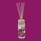 Glass reed diffuser with red botanical pieces and a wooden cap.