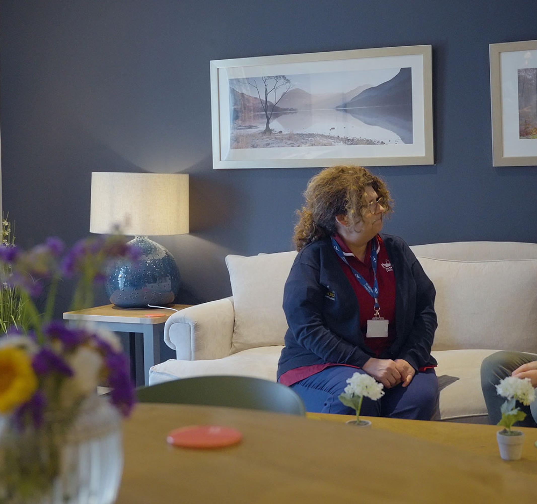 Woman in uniform talks to a man on a white sofa in a modern living room.