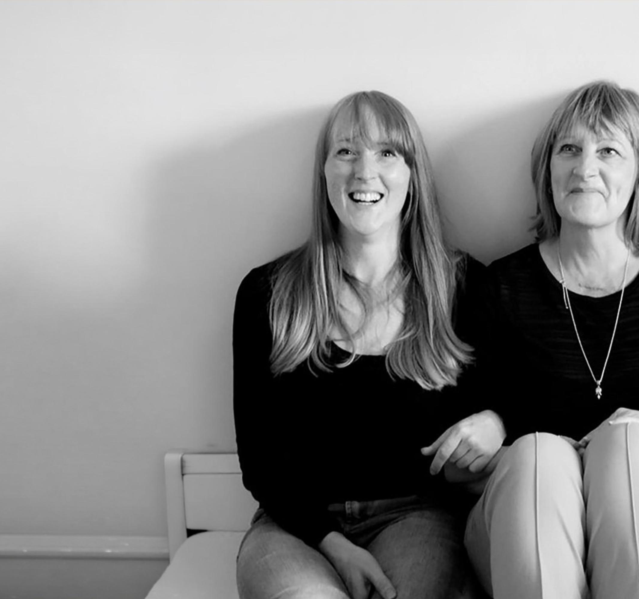 Three smiling women sit together, possibly mother and daughters. Black and white photo.