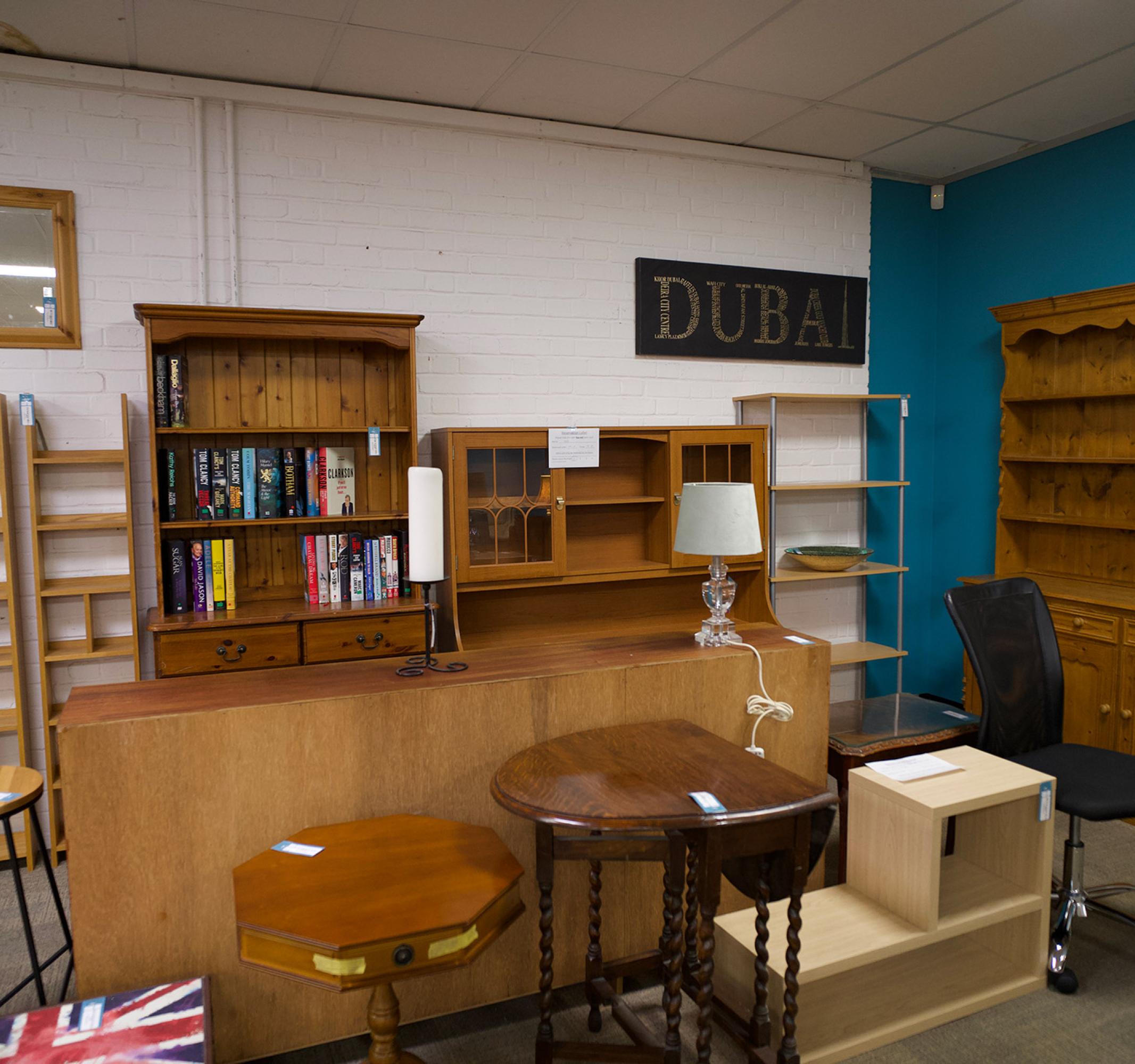 Room with various wooden furniture, including bookshelves, tables, and cabinets, in a retail setting.