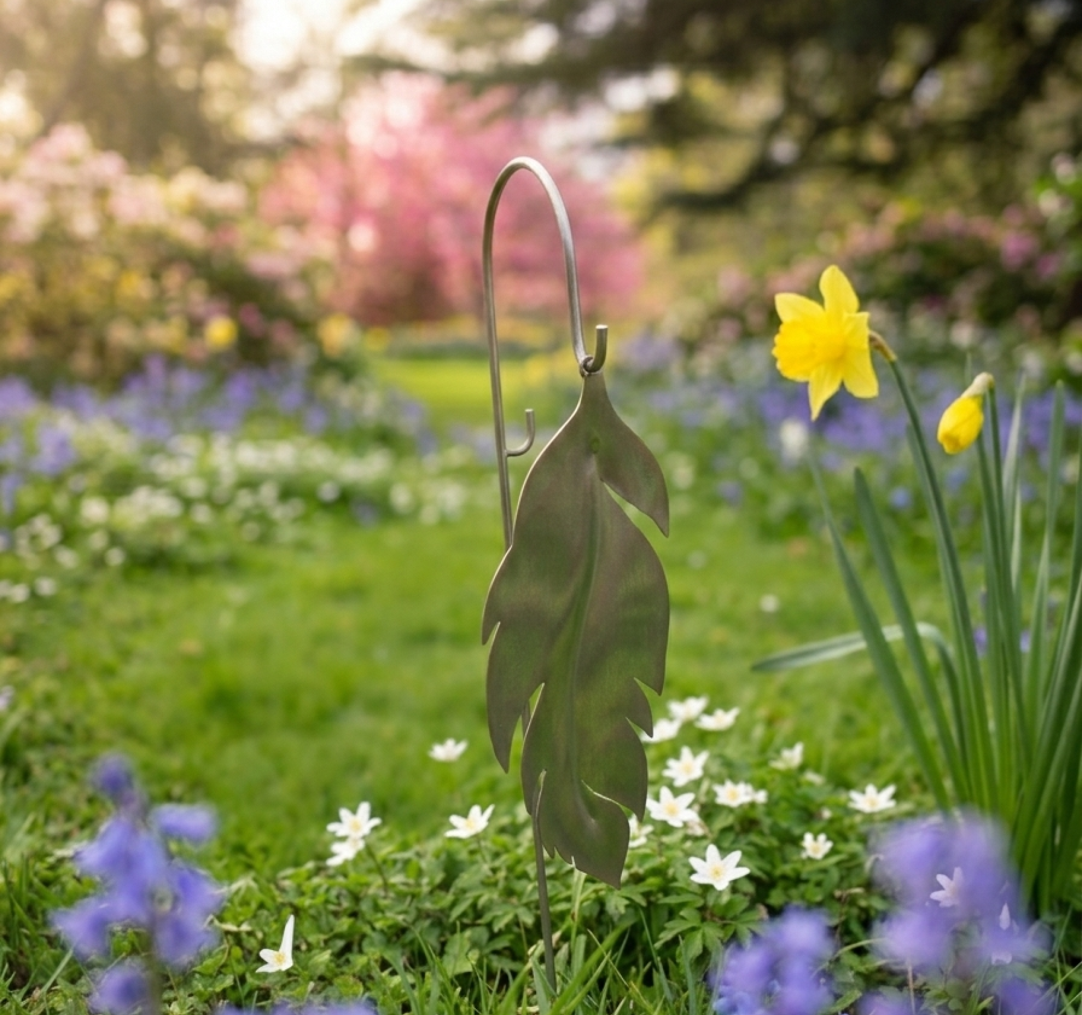 Metal leaf garden art among colorful spring flowers like daffodils and purple bells.