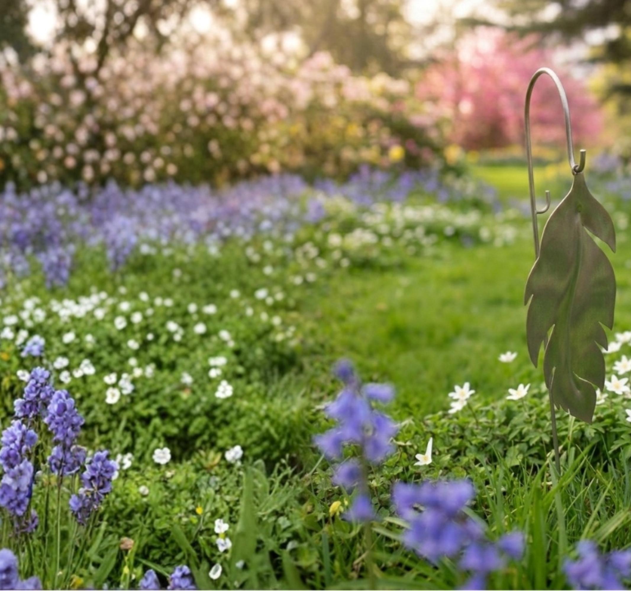 Vibrant spring garden with purple and white flowers, a metal leaf sculpture, and a yellow daffodil.