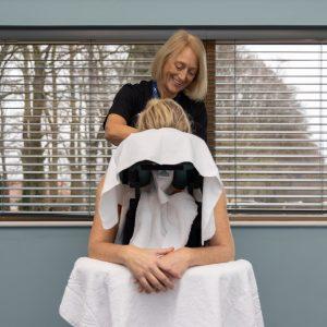 Smiling masseuse massages a client's neck and shoulders in a portable chair.