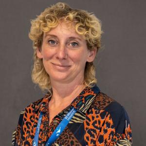 Smiling woman with blonde curly hair, wearing a patterned shirt and blue lanyard.