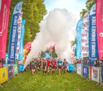 Runners emerge from smoke at the start of a Thames Bridges Trek.