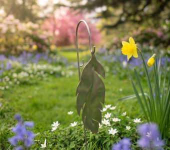Metal leaf garden decoration among blue, white, and yellow flowers in a sunny spring garden.