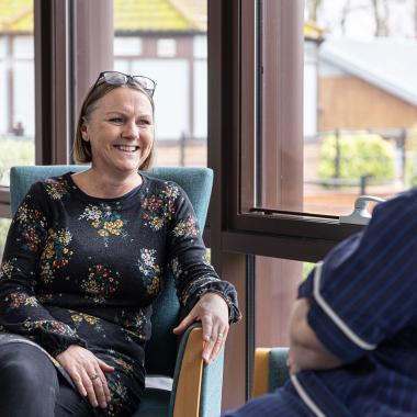 Smiling woman in floral dress talks with person in blue uniform.