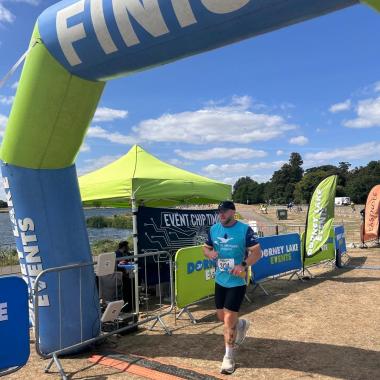Man runs past a blue and green "FINISH" line arch at an outdoor race.