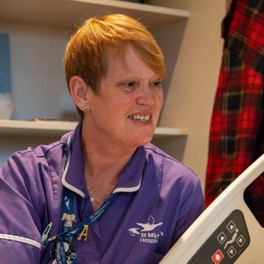 Smiling red-haired nurse in purple scrubs in a hospital room.
