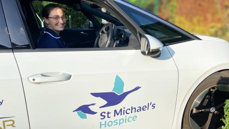 Smiling woman in uniform in a white St Michael's Hospice car.