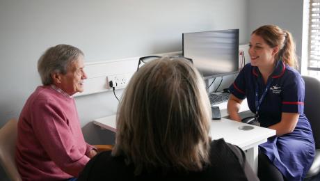 Nurse smiles at elderly man during a consultation; third person listens.