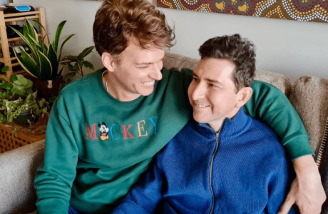 Two smiling men look lovingly at each other while sitting on a couch.