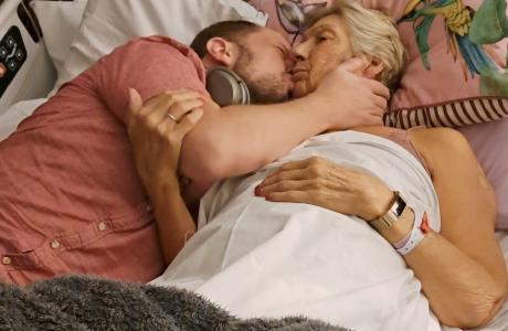 Man kisses older woman on cheek in hospital bed.