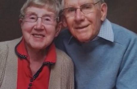 Happy elderly couple smiling. Woman in red top, man in blue sweater.