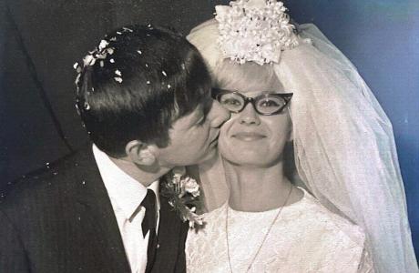 Vintage photograph of a groom kissing his smiling bride wearing a veil and glasses.