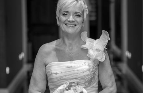 Smiling woman in a wedding dress holding a bouquet in a hallway.
