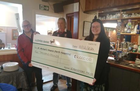 Three smiling people hold a large novelty check for £2,000 in a pub setting.