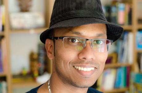 Sari: Smiling man in a black fedora and glasses with bookshelves in the background.