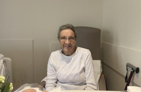 Smiling elderly woman with glasses in a hospital room.