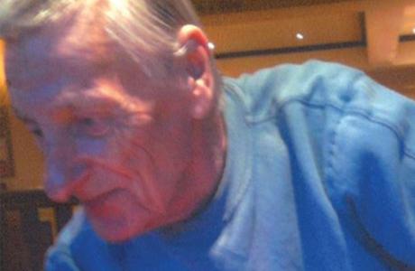 Older man with gray hair wearing a blue shirt, looking down.