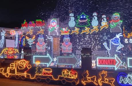 Colorful Christmas light display at night with Santa, reindeer, snowmen, and falling snow.