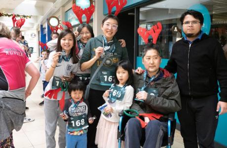 Festive group with reindeer antlers and race bibs, one adult in a wheelchair, in a mall.