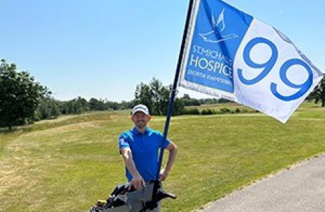 Man in blue t shirt and cream shorts on golf course holding golf clubs