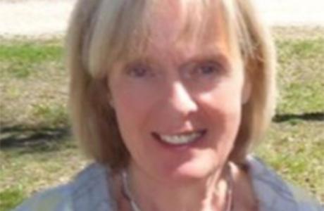 Smiling blonde woman with short hair and a silver necklace, outdoors.