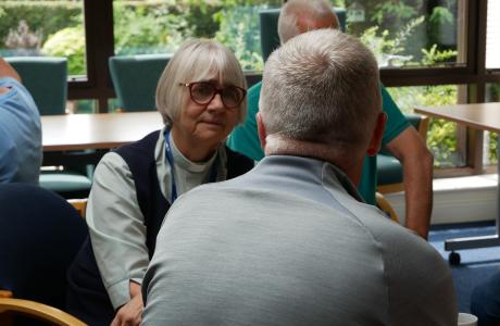 Woman with blonde hair and glasses attentively listens to a man in a meeting room.