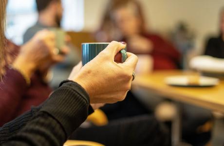 Close-up of hands holding a teal mug, blurred people in the background.