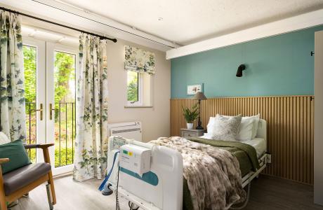 Comfortable room with green bedding, adjustable bed, teal wall, and bright French doors.