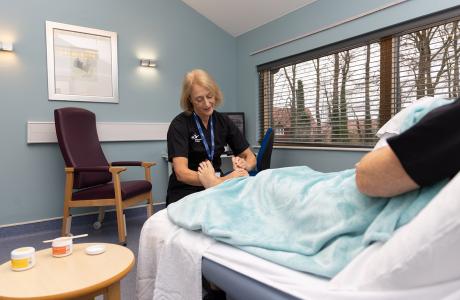 Therapist giving a foot massage to a person lying on a bed in a light blue room.