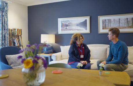 Caregiver and man converse on a white sofa in a modern living room.