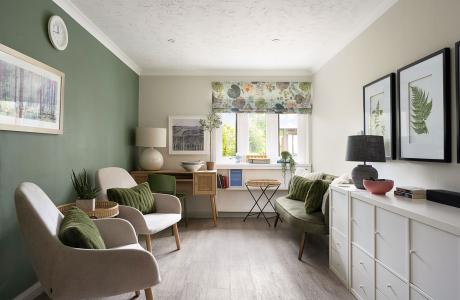 Stylish room with a green accent wall, two armchairs, floral window blind, and white storage cabinet.