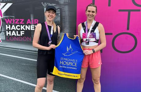 Two smiling women with medals hold up a Serenmobile Hospice running vest after a race.