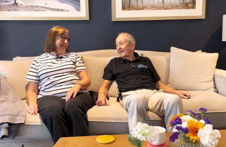 Elderly couple happily talking on a couch in a living room with flowers.