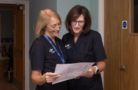 Two women in dark uniforms smile as they review a document.