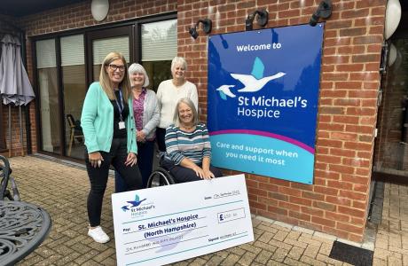 Five women, one in a wheelchair, hold a large check outside St Michael's Hospice.