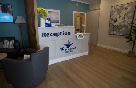 Bright hospice reception with "Reception" desk, armchairs, and art.
