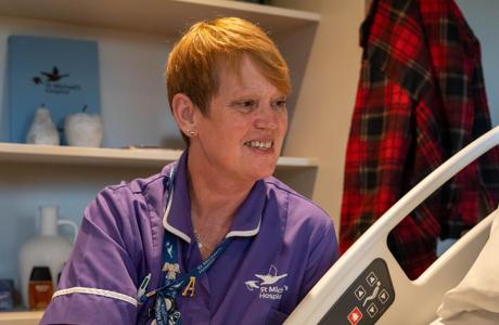 Smiling red-haired nurse in purple scrubs in a hospital room.