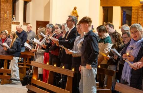 Congregation standing and singing from papers in a church, some holding lit candles.
