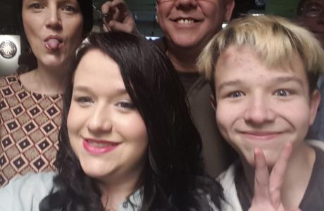 Group selfie: Woman with tongue out, smiling man, smiling woman, and person making peace sign.