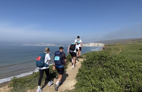 People walking away from the camera on a coastal path the the blue sky and sea scene in the background
