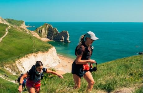 Two people climbing a small incline on the Jurassic coast path with the sea in the background
