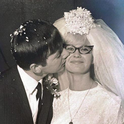 Vintage photograph of a groom kissing his smiling bride wearing a veil and glasses.