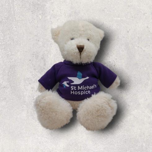 White teddy bear wearing a purple shirt with "St Michael's Hospice" logo.