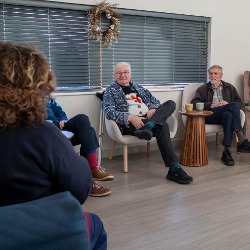Diverse group of adults in a casual lounge setting, one man in a snowman sweater smiling.