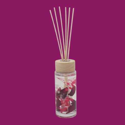 Glass reed diffuser with red botanical pieces and a wooden cap.