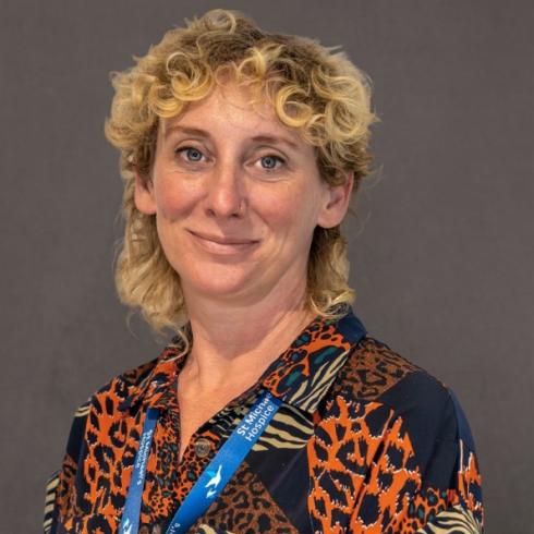 Smiling woman with blonde curly hair, wearing a patterned shirt and blue lanyard.
