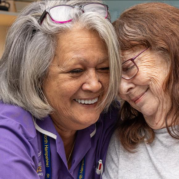 Photograph: Smiling caregiver in purple uniform embracing an older woman.